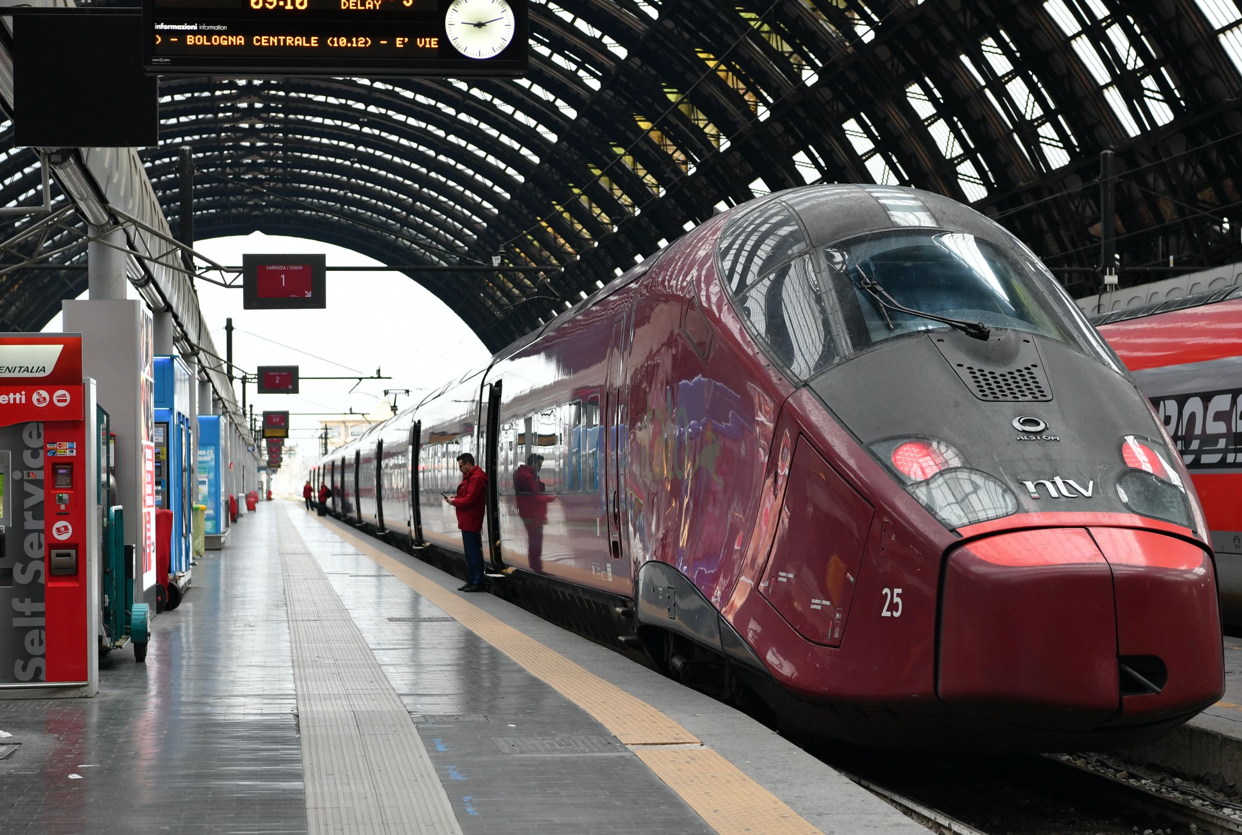 An Italo high-speed train waits at a platform in Milano Centrale station with Bologna Centrale on the departure board.