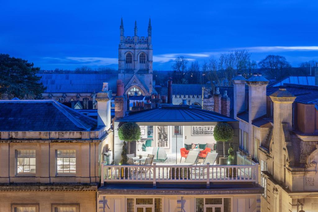 A rooftop terrace with outdoor seating overlooks a city skyline featuring a stone church tower at twilight.