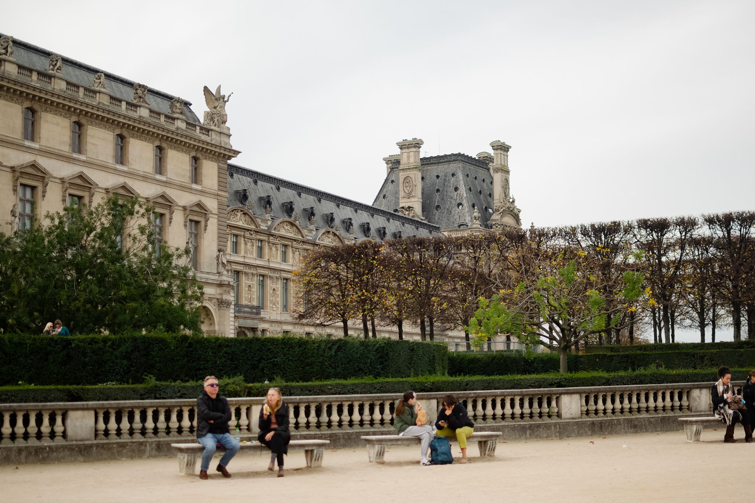 Tourists sit on benches in the Tuileries Garden with the Louvre Museum in Paris.