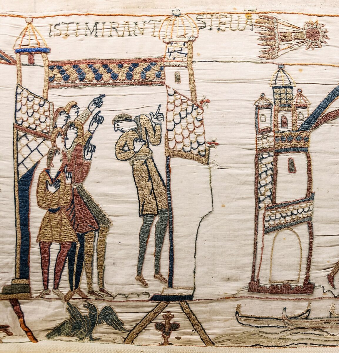 An embroidered scene depicts figures pointing toward a star in the sky above buildings with Latin text overhead.