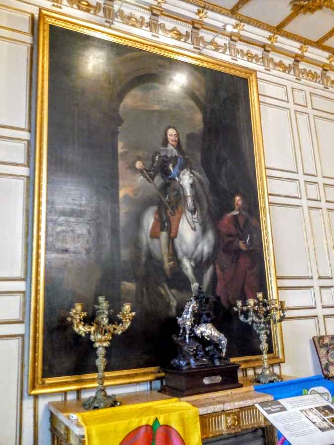 A large framed oil painting of a man on a white horse hangs on a paneled wall above a table with decorative candelabras.