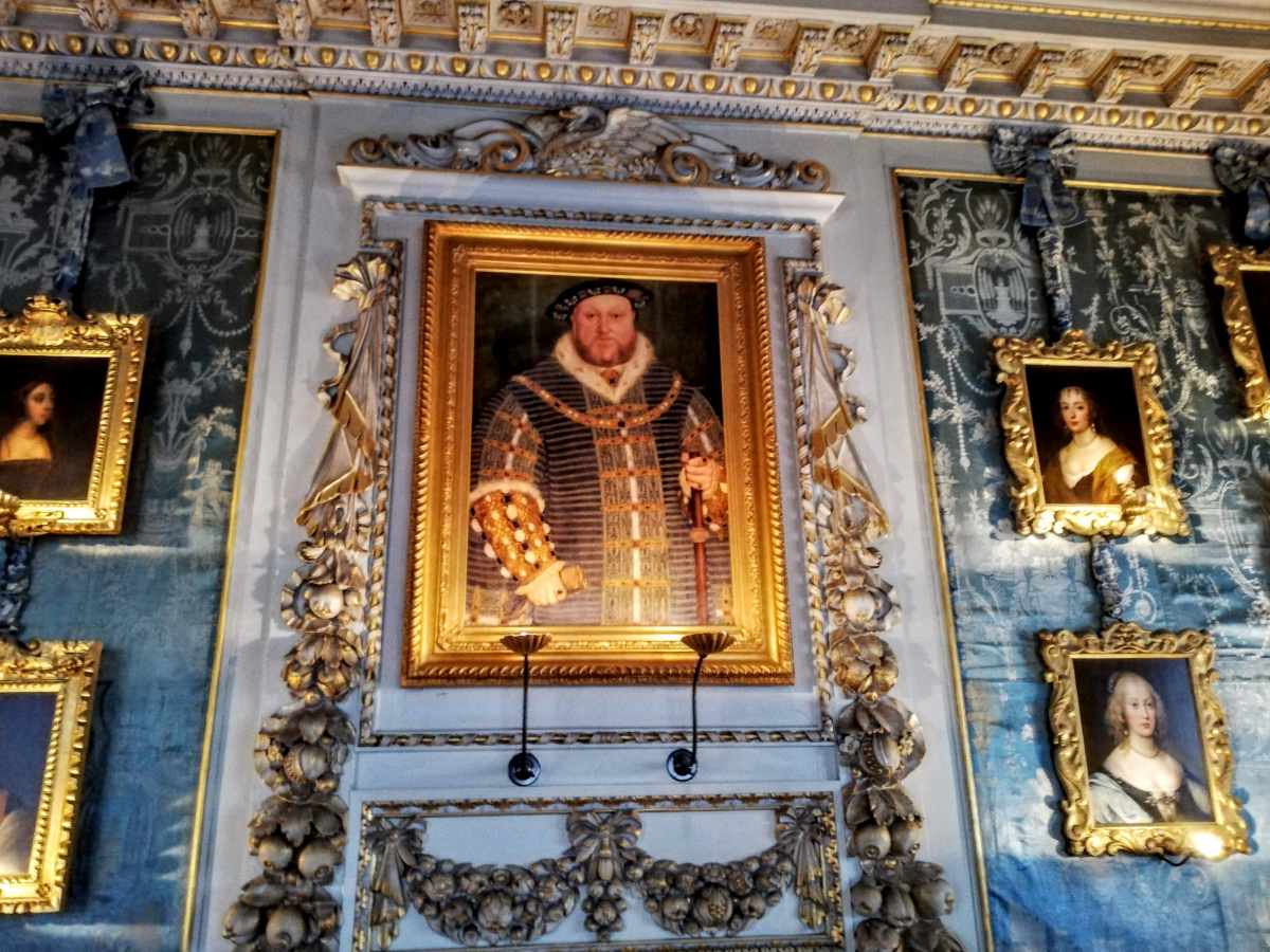 A large portrait of a bearded man in historical attire hangs on a blue patterned wall surrounded by smaller portraits.