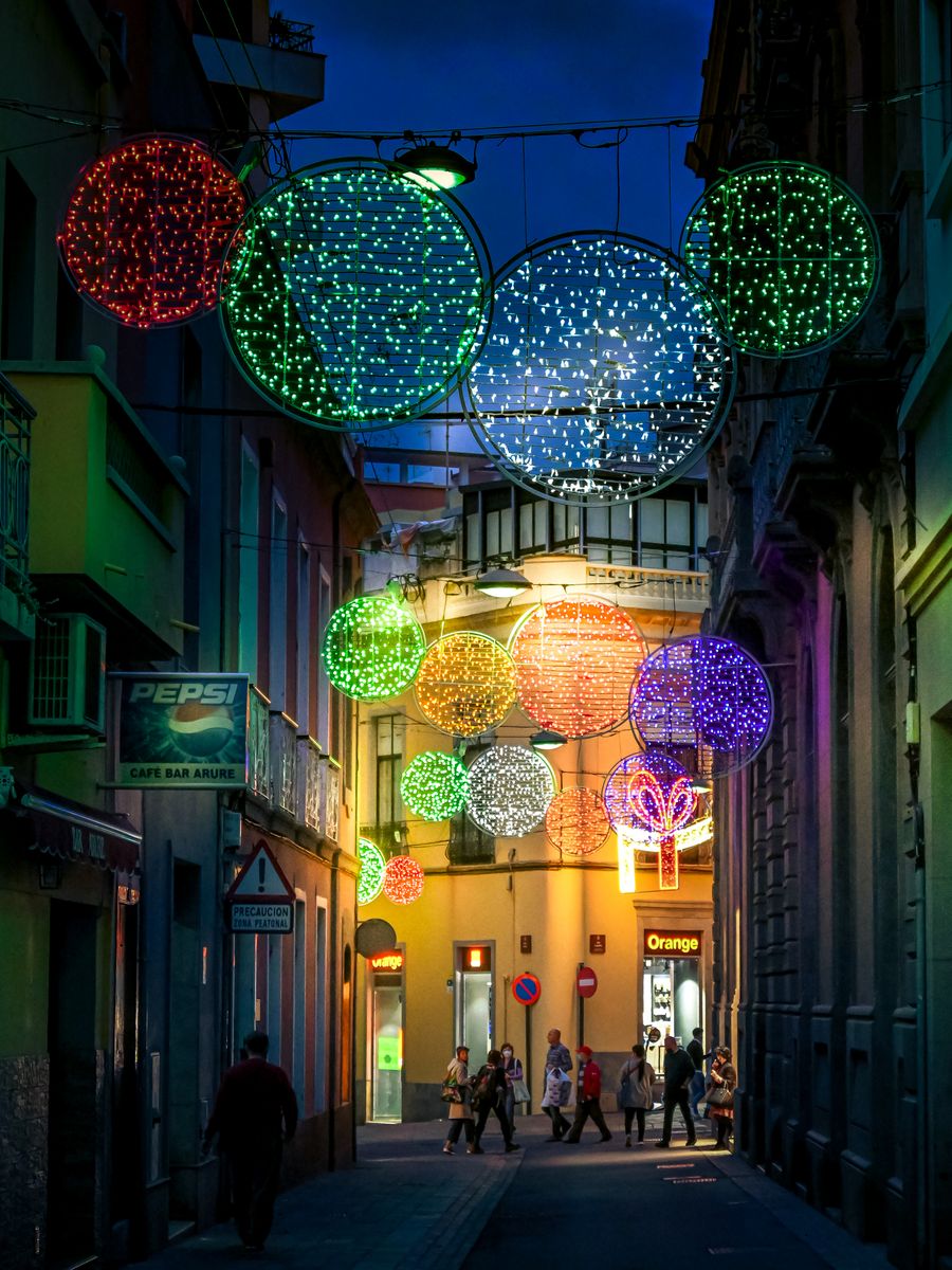 A lively street in Santa Cruz de Tenerife adorned with colorful Christmas lights at night.