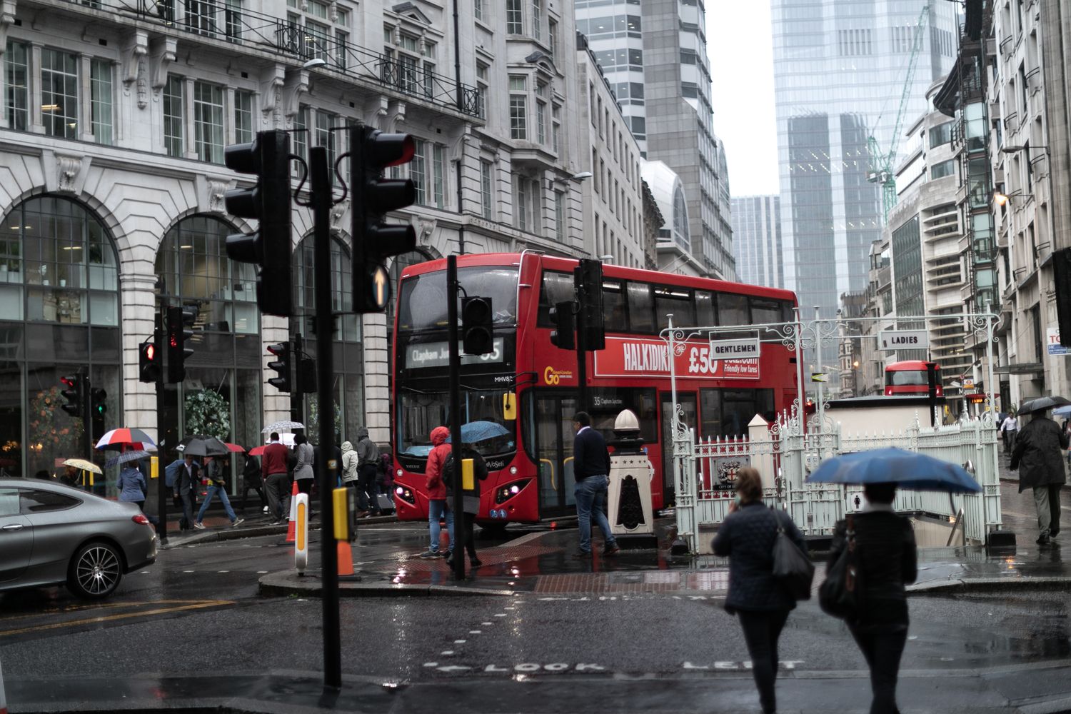 A rainy London street scene featuring iconic red double decker buses and pedestrians with umbrellas.