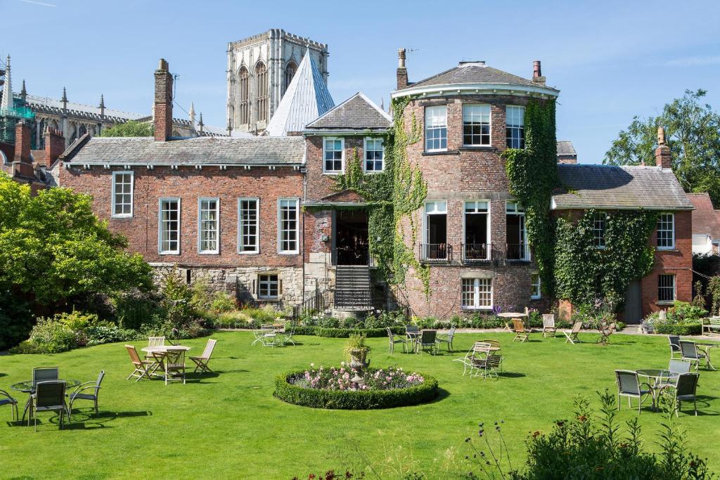 A brick building with ivy and a large lawn featuring a circular flower bed and scattered outdoor tables and chairs.