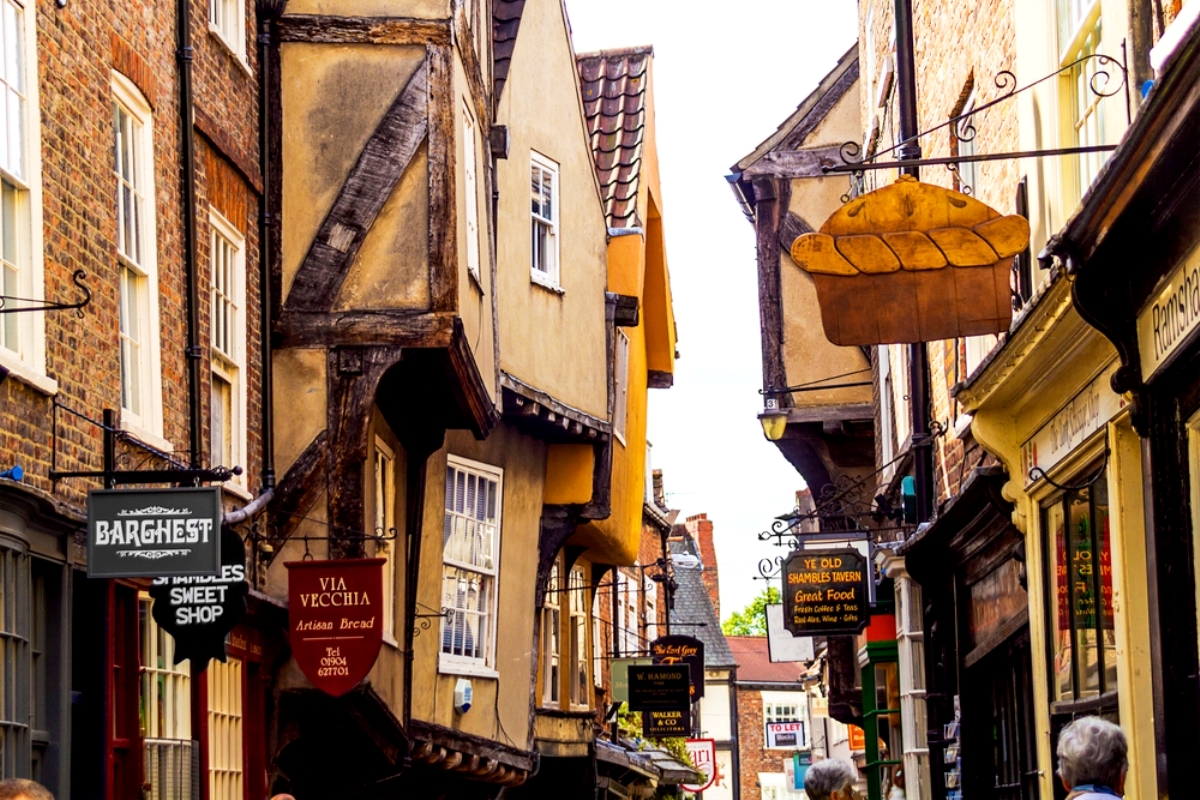 A narrow street lined with historic timber-framed buildings and various hanging shop signs.