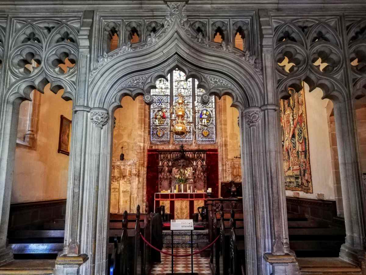 An ornate stone archway frames a church interior with wooden pews, a central altar, and stained glass windows.