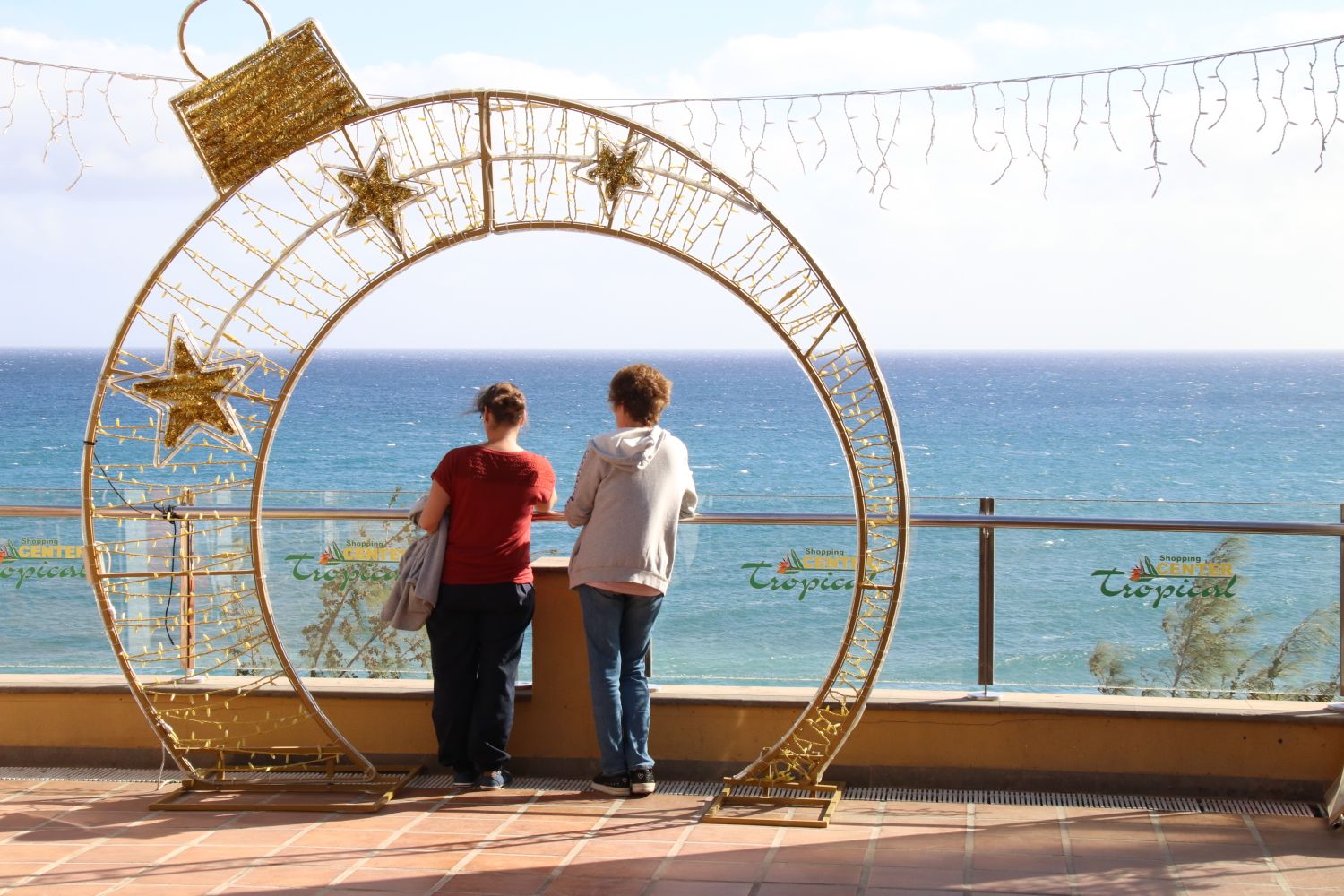 Two people admire the ocean view through a decorative frame at Playa del Ingles.