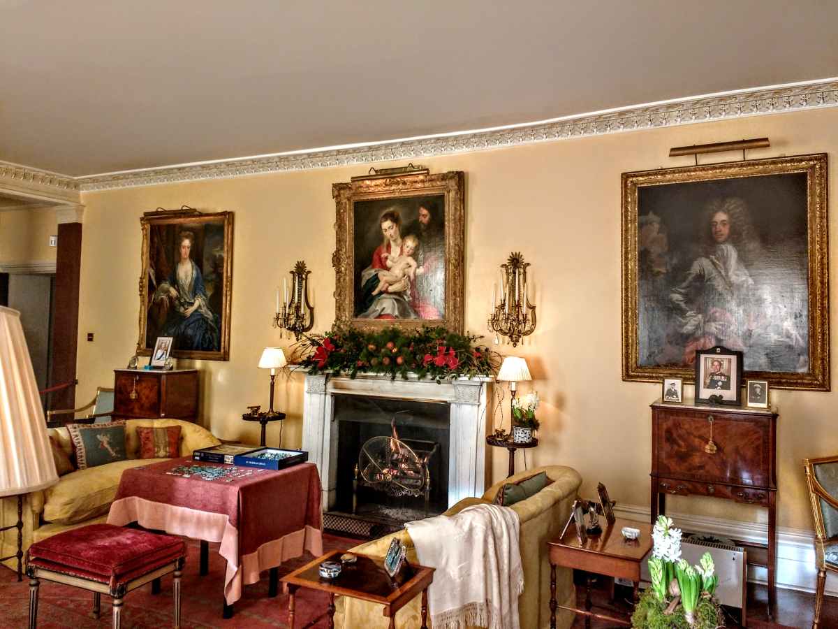 A cozy living room features a fireplace decorated with greenery, flanked by large framed portraits on a pale yellow wall.