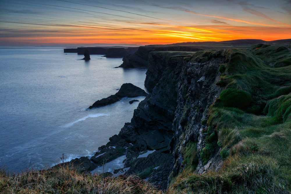 A sunset glows over rugged coastal cliffs overlooking the ocean.