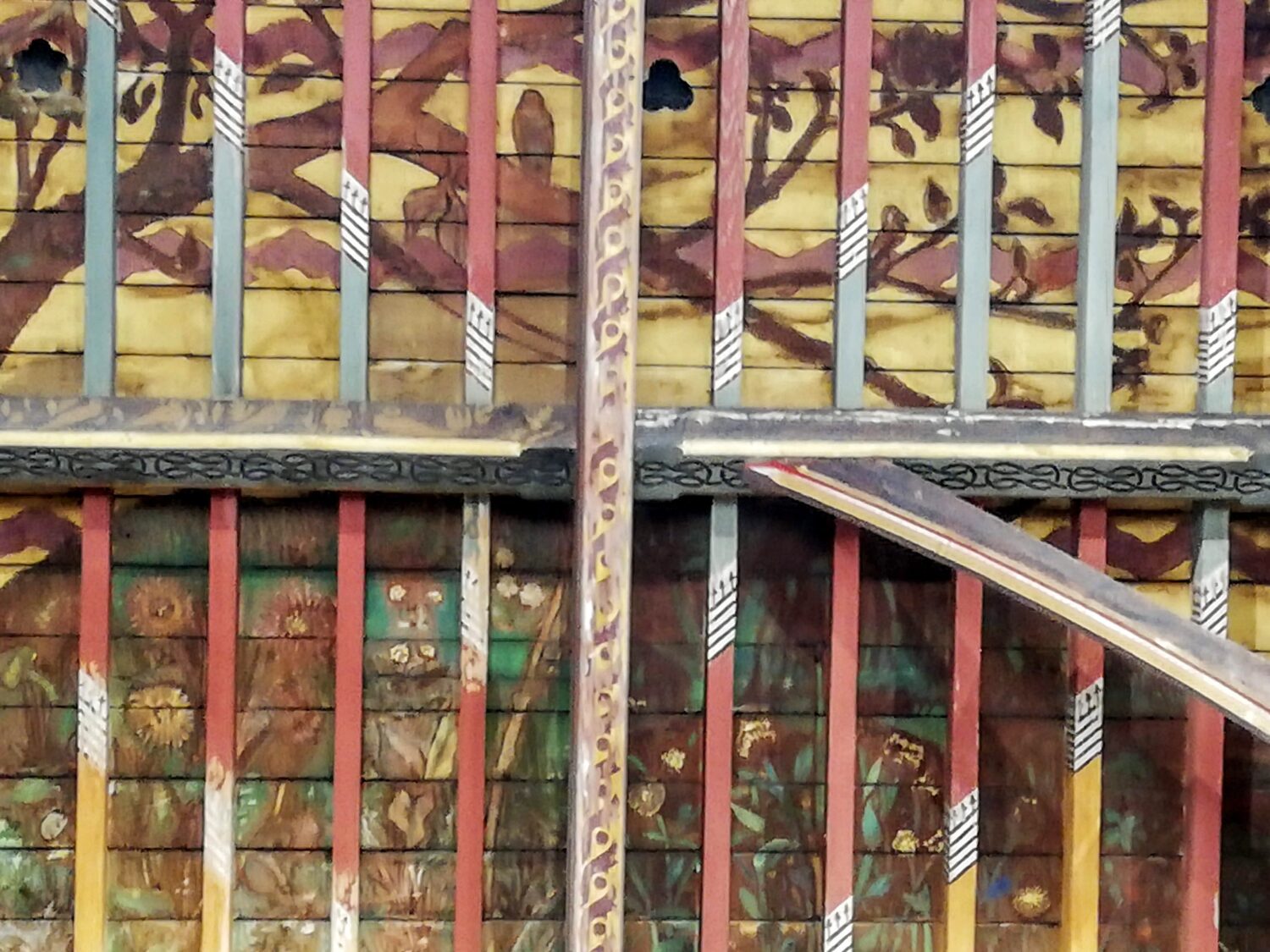 A painted wooden ceiling features panels with floral and tree motifs separated by vertical and horizontal beams.